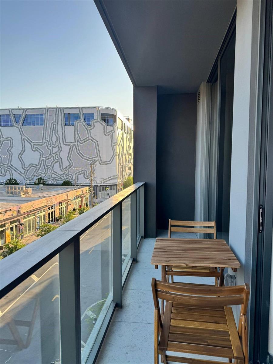 A balcony with a wooden table and chairs overlooks a street and a patterned building — 2700 NW 2nd Ave # 305, Miami FL 33127, MIAMI, FL