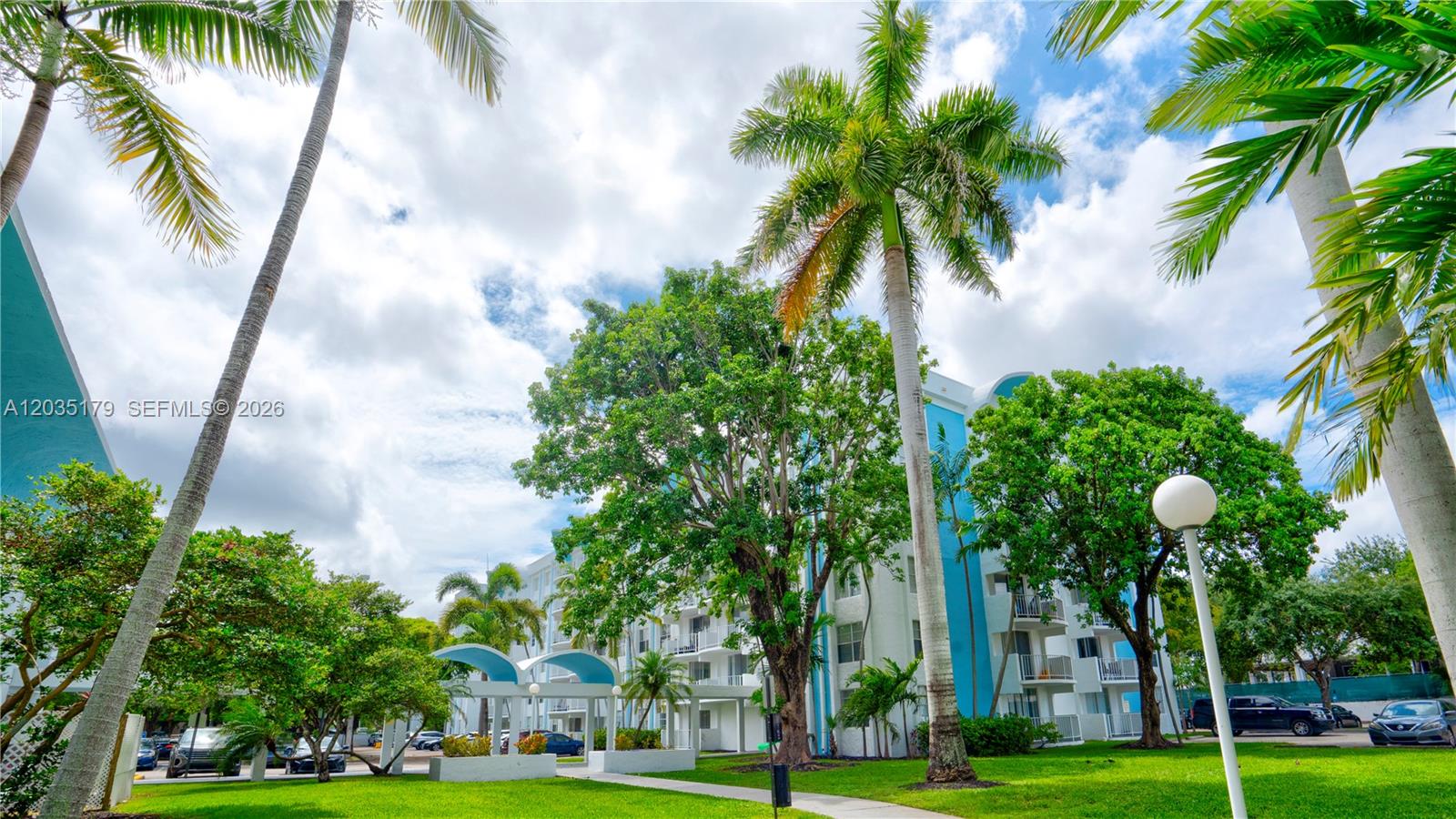 A multi-story apartment building with blue accents is surrounded by palm trees and landscaping — MIAMI, FL