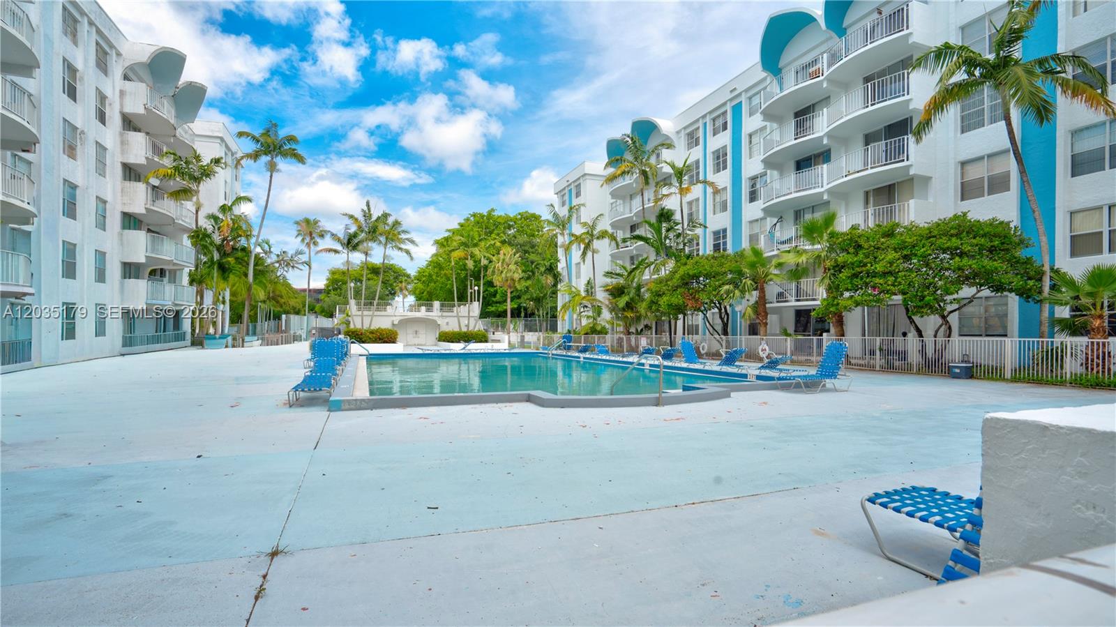 A swimming pool sits between two multi-story apartment buildings with balconies and palm trees — MIAMI, FL