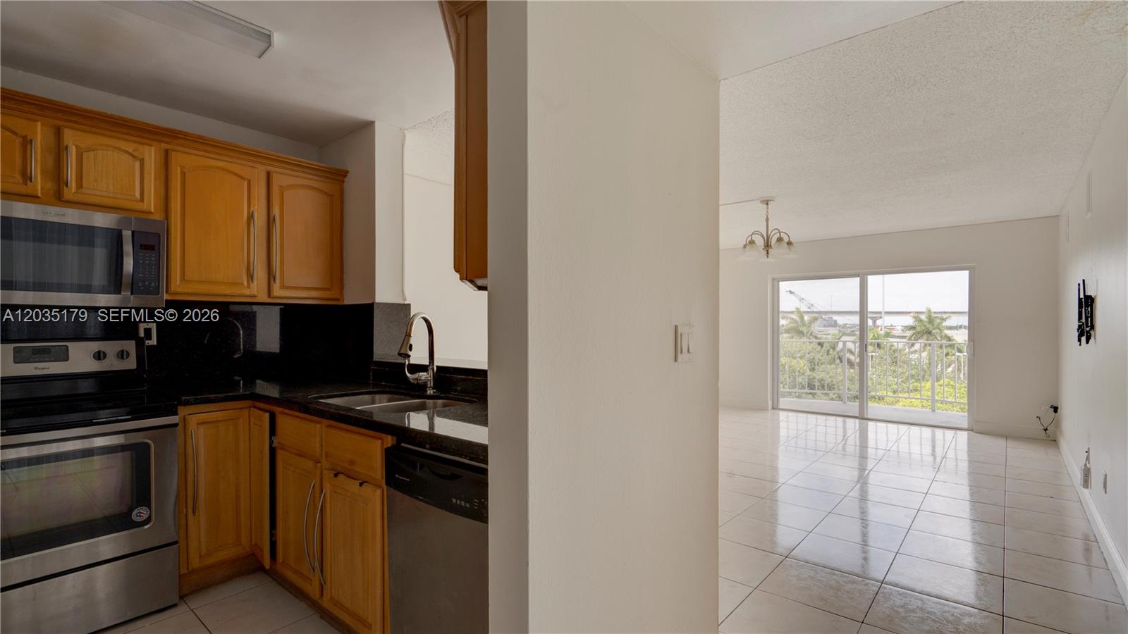 A kitchen with wood cabinets and black countertops opens into a bright, tiled living area — MIAMI, FL