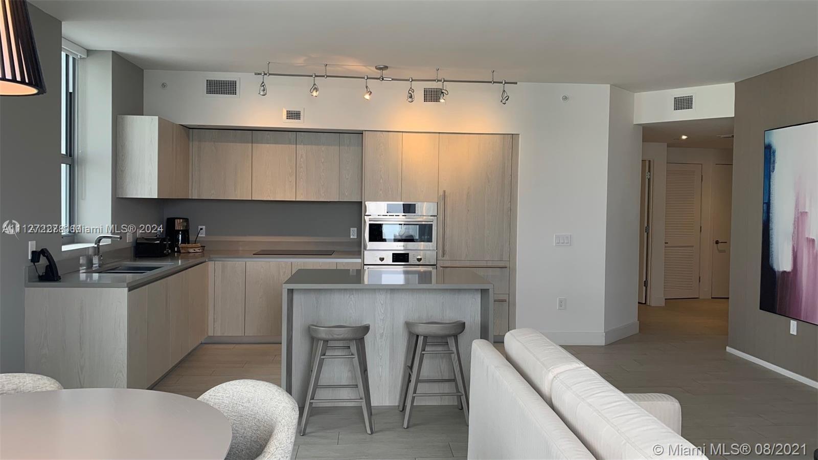 A modern kitchen features light wood cabinetry, a central island with bar stools, and stainless appliances — 4010 S Ocean Dr # R401, Hollywood FL 33019, HOLLYWOOD, FL