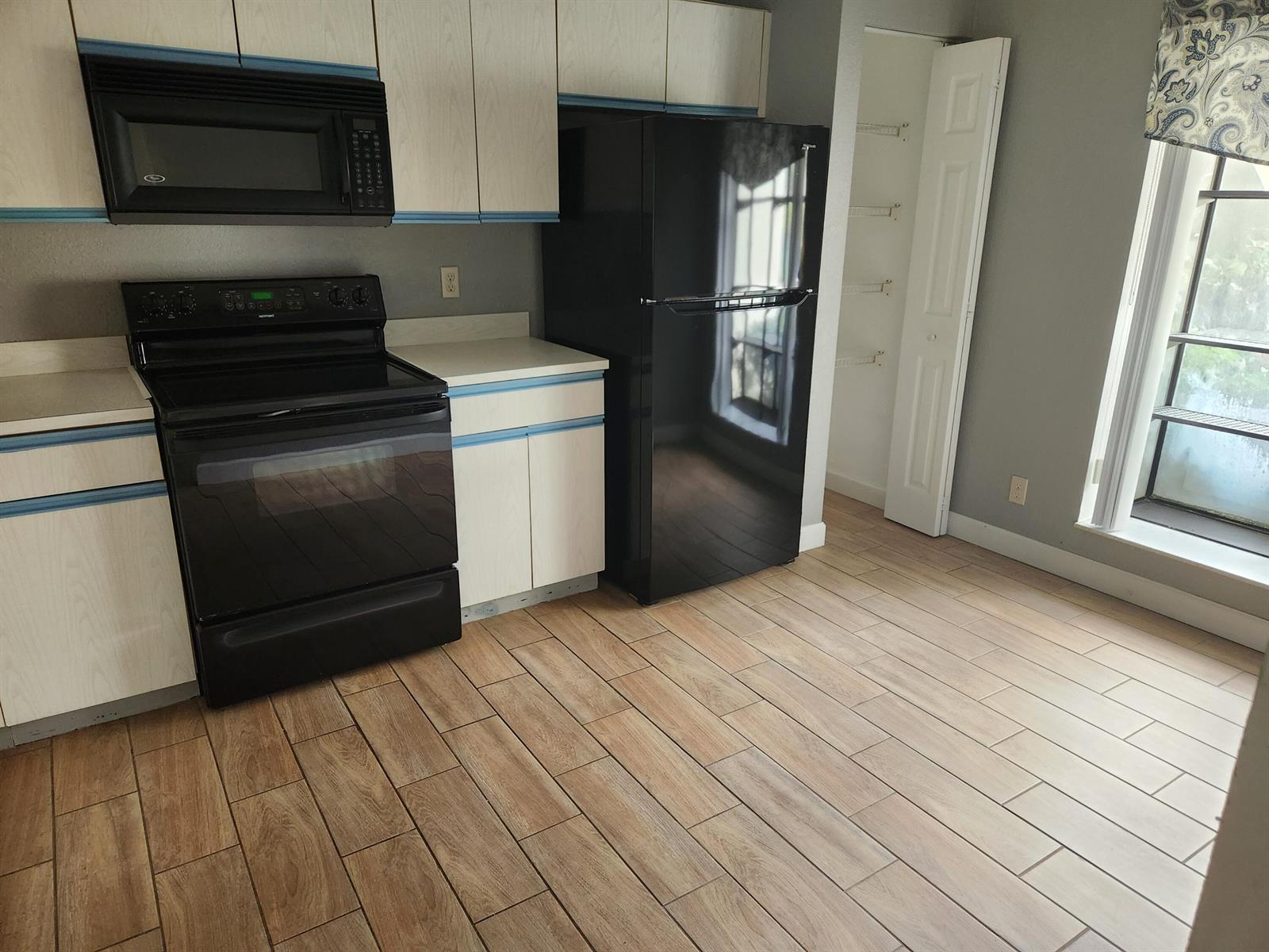 A kitchen features light wood-grain cabinets, black appliances, and wood-look tile flooring — 3345 Lucerne Park Drive, FL 33467, FL