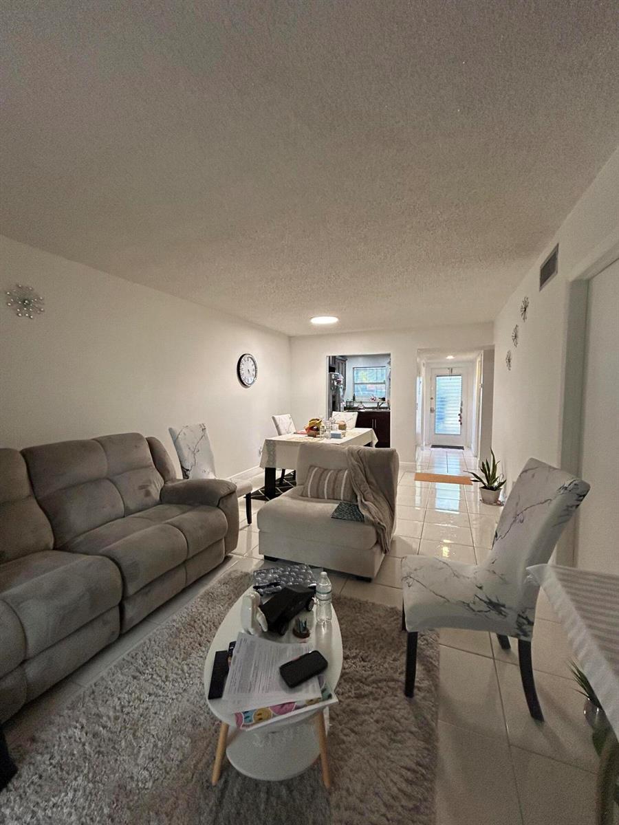 A living room with a grey sofa, white armchair, dining table, and light tile flooring — 6600 Royal Palm Boulevard # 103b, Margate FL 33063, MARGATE, FL