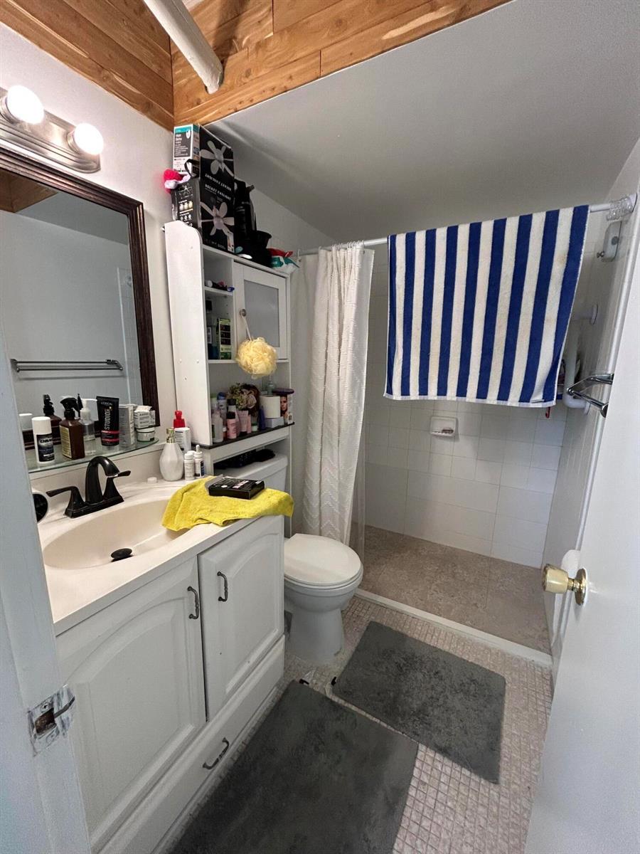 A bathroom features a white vanity, a toilet, and a walk-in shower with a curtain — 6600 Royal Palm Boulevard # 103b, Margate FL 33063, MARGATE, FL