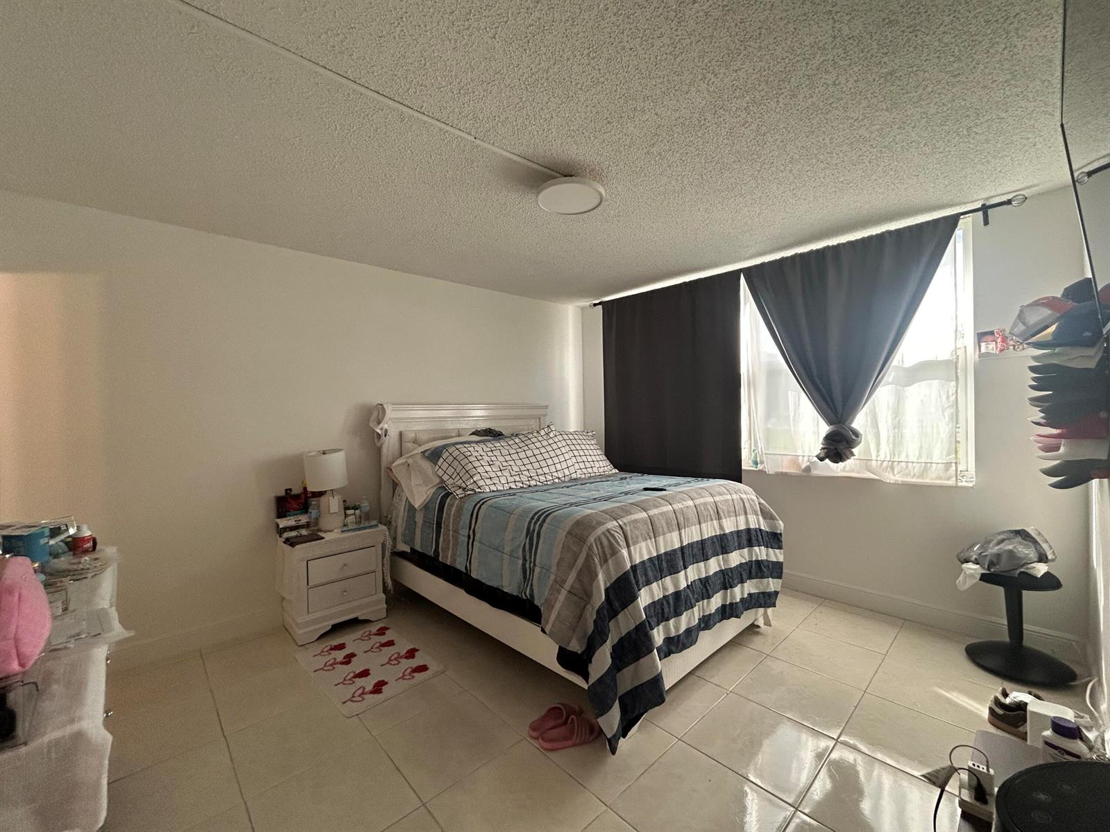 A bedroom features a bed with a striped comforter, white tile floors, and a window — 6600 Royal Palm Boulevard # 103b, Margate FL 33063, MARGATE, FL