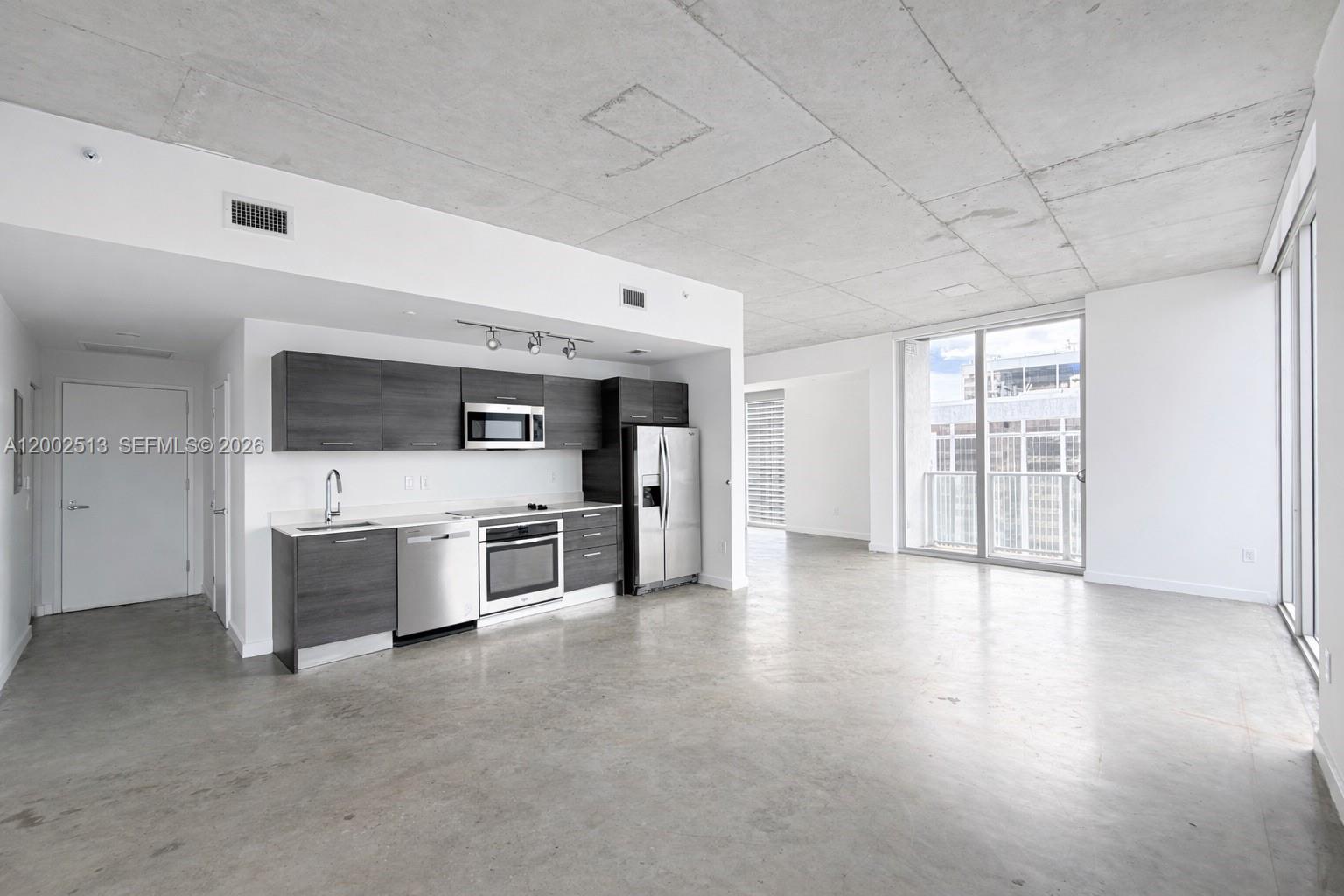 A modern kitchen with dark cabinetry and stainless steel appliances sits in an open-concept space — 151 SE 1st St # 3001, Miami FL 33131, MIAMI, FL
