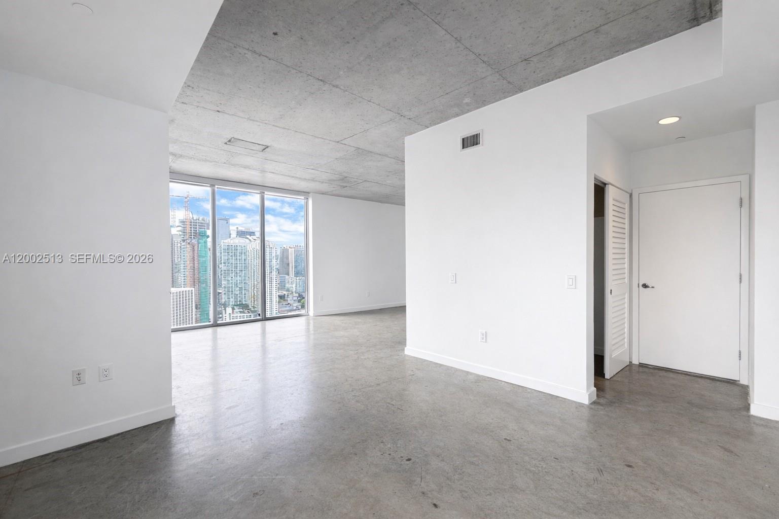 An empty room features concrete floors and ceilings with floor-to-ceiling windows overlooking a city skyline — 151 SE 1st St # 3001, Miami FL 33131, MIAMI, FL