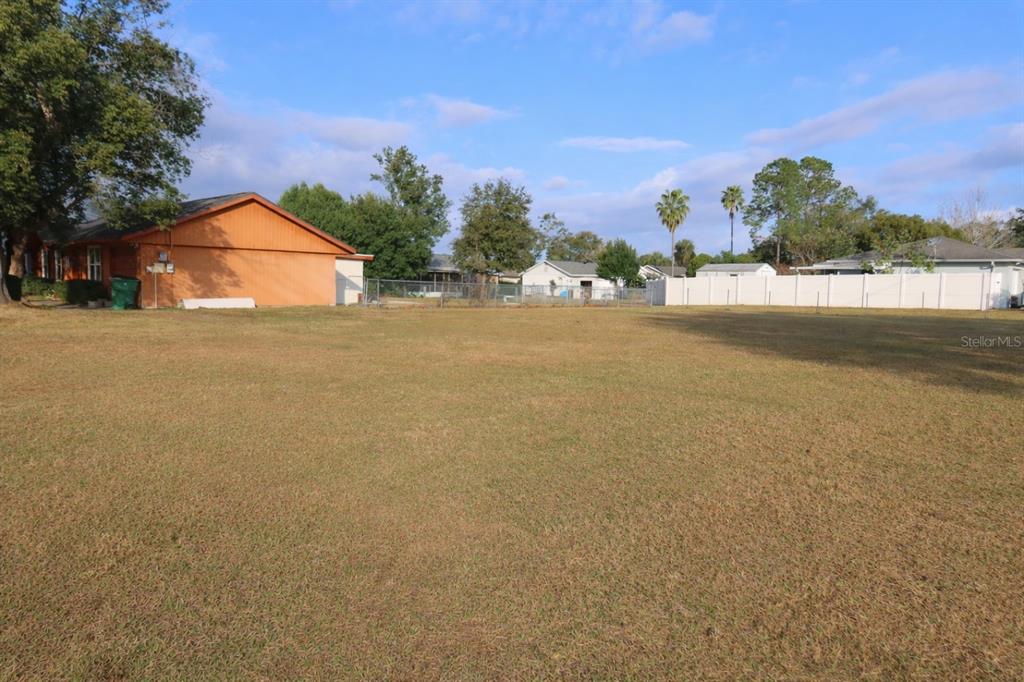 A large, flat, grassy lot sits in front of a house with orange siding — NORTH AVENUE, ZEPHYRHILLS, FL