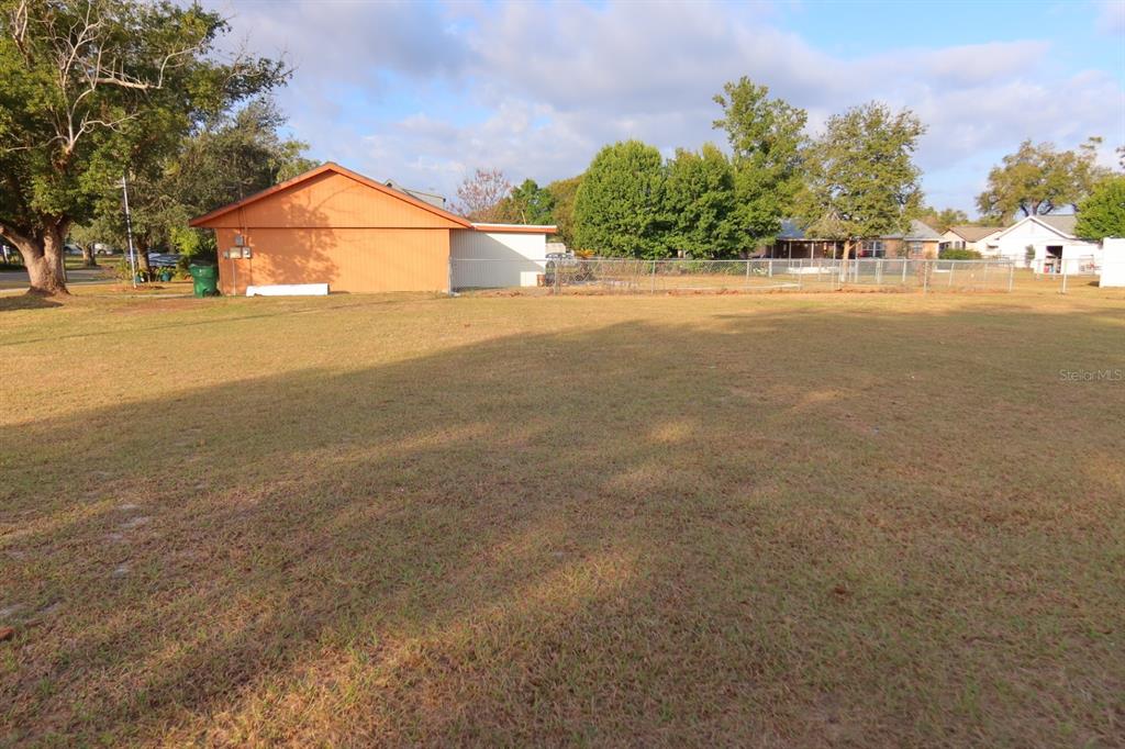 A large, grassy vacant lot sits in front of a single-story house with orange siding — NORTH AVENUE, ZEPHYRHILLS, FL