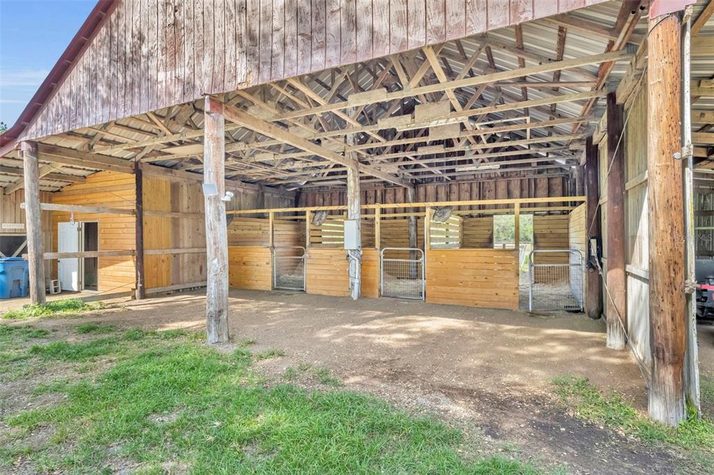 An open-air barn features several horse stalls with wooden walls and metal gates — 430 CYPRESS ISLES ROAD, OSTEEN, FL