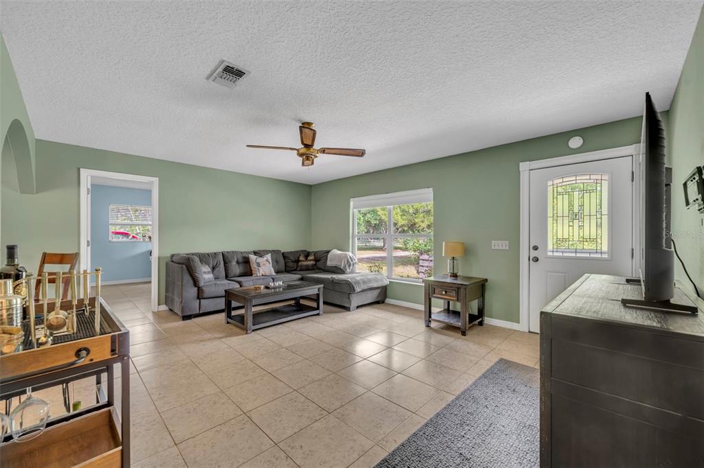 A living room features sage green walls, tile flooring, a gray sectional sofa, and a television — 430 CYPRESS ISLES ROAD, OSTEEN, FL