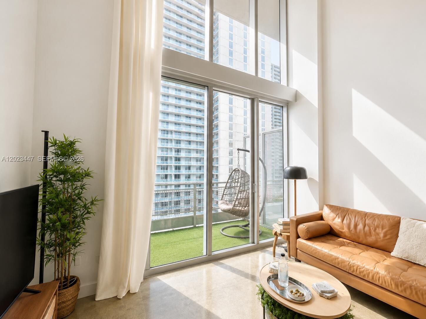 A living room features a leather sofa, floor-to-ceiling windows, and a balcony with artificial turf — 690 SW 1st Ct # 2314, Miami FL 33130, MIAMI, FL