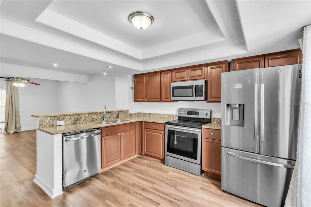 A kitchen features wood cabinets, granite countertops, stainless steel appliances, and light wood flooring — 3303 BRIGADOON DRIVE, CLEARWATER, FL