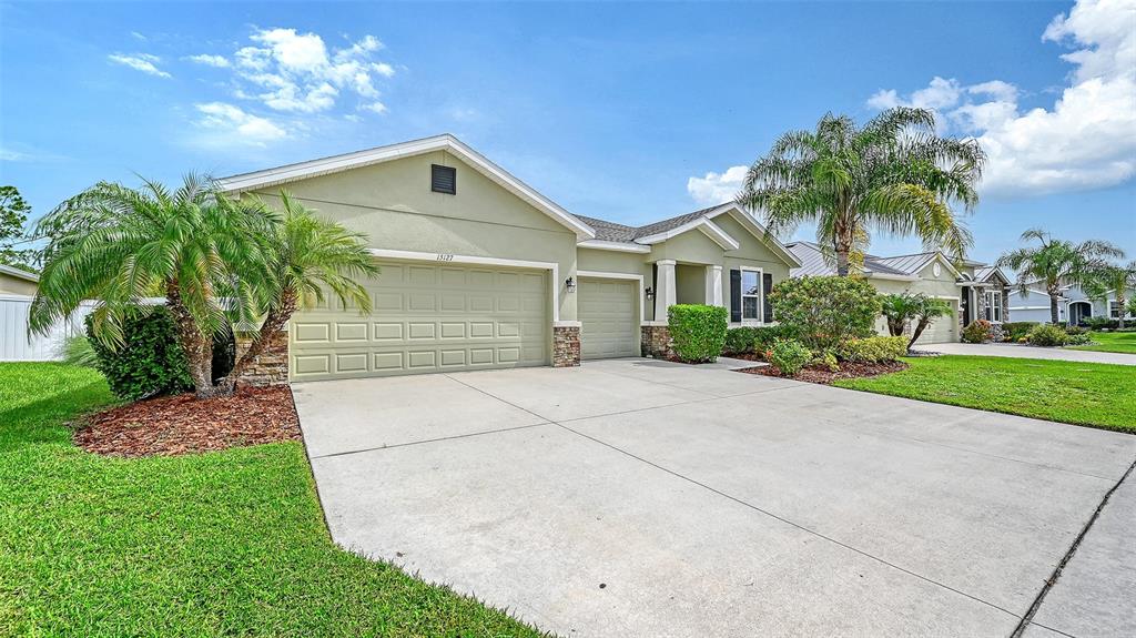 A single-story house with a two-car garage, light green stucco, and palm trees in front — 15127 LAS OLAS PLACE, BRADENTON, FL