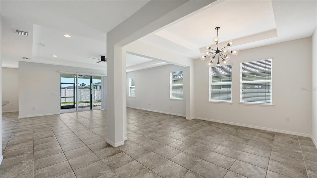 An open-concept dining and living area features tile flooring, a tray ceiling, and a chandelier — 15127 LAS OLAS PLACE, BRADENTON, FL