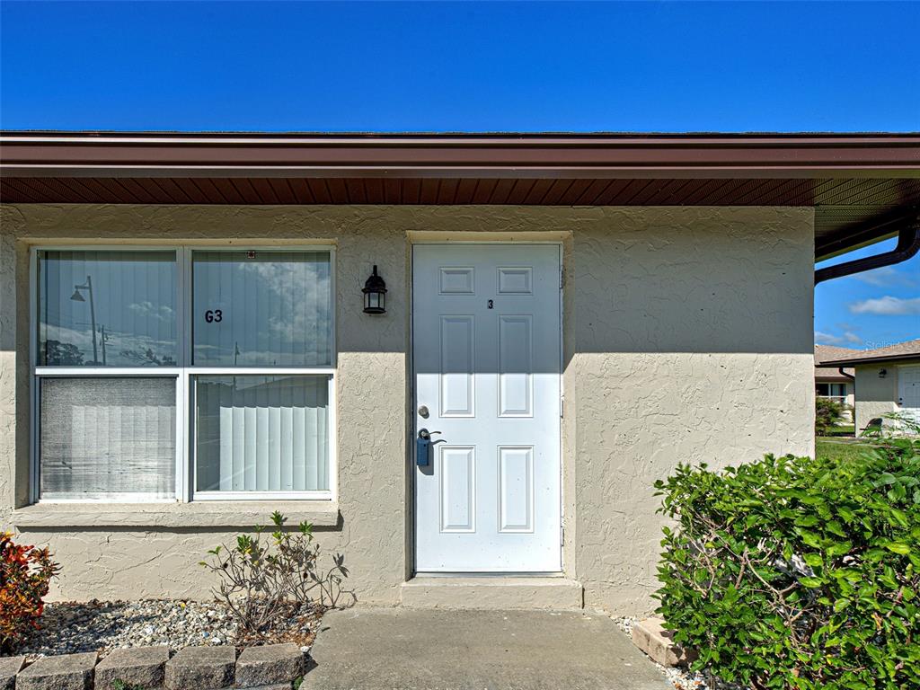The exterior of a single-story building features a white door, a window, and landscaping — 21150 GERTRUDE AVENUE UNIT G3, PORT CHARLOTTE, FL
