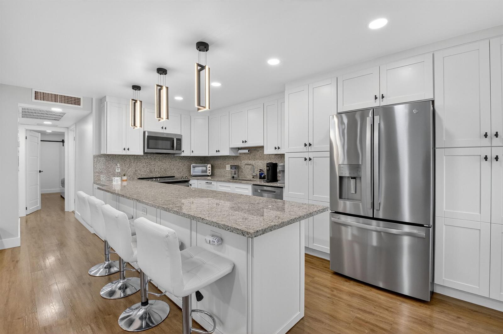 A kitchen features white cabinets, granite countertops, stainless steel appliances, and three bar stools — 3005 Guildford A, Boca Raton FL 33434, BOCA RATON, FL