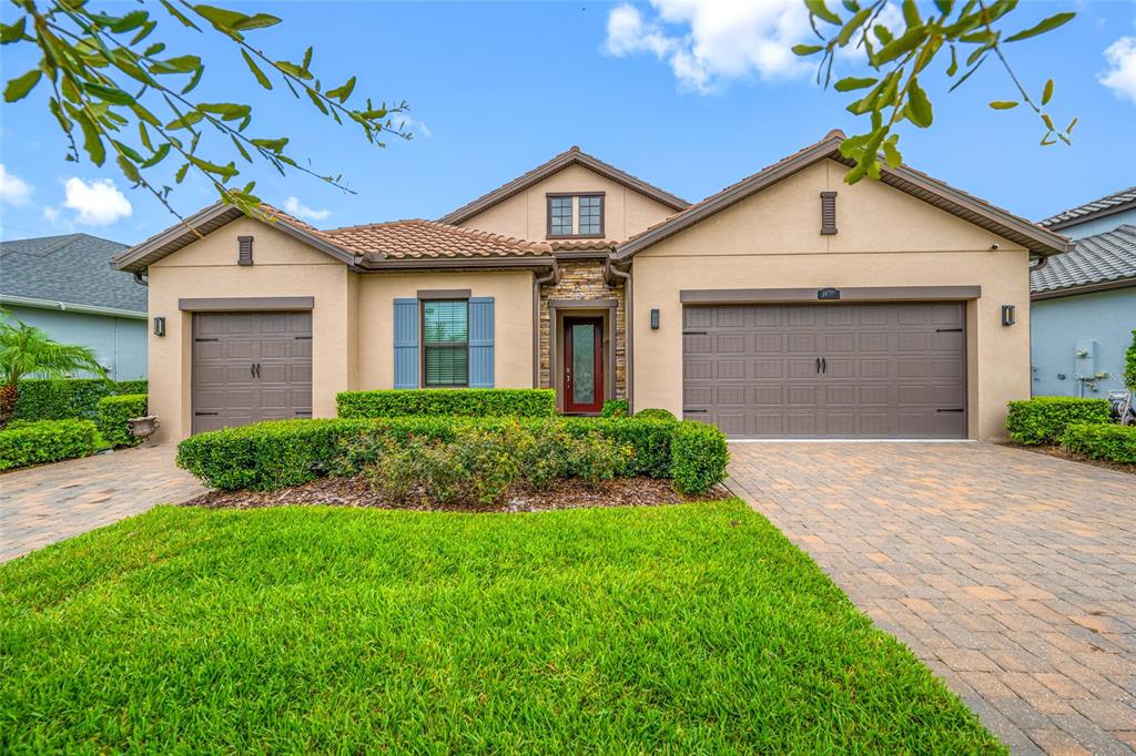 A single-story house with a tan stucco exterior, two garage doors, and a paved driveway — 18308 LEAFMORE STREET, LUTZ, FL