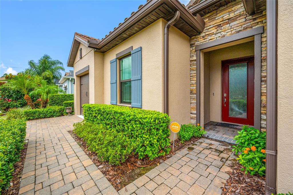 A paved walkway leads to the front entrance of a house with tan stucco walls — 18308 LEAFMORE STREET, LUTZ, FL