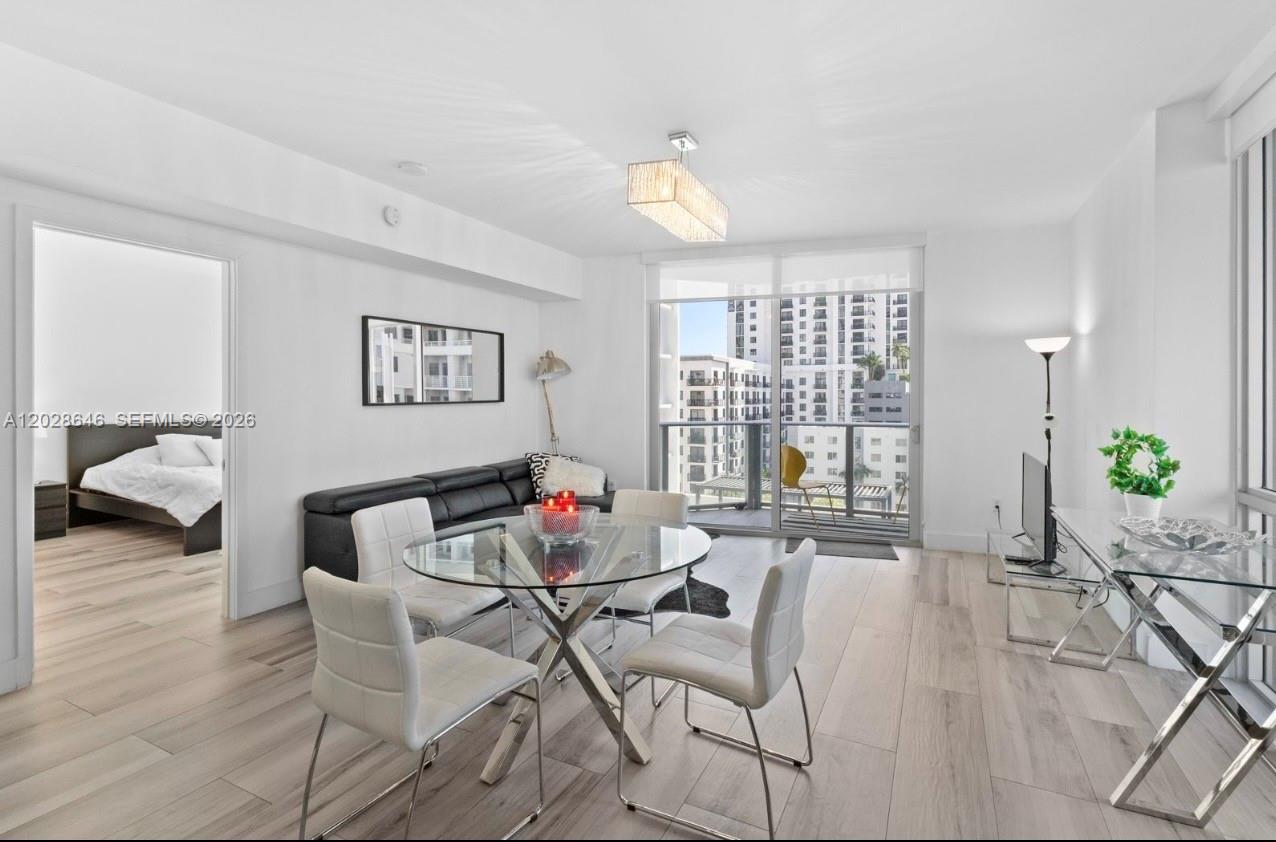 A bright living and dining area features light wood floors, a glass table, and balcony access — 1010 SW 2nd Ave # 609, Miami FL 33130, MIAMI, FL