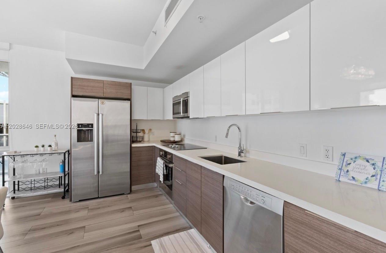 A modern kitchen features white upper cabinets, wood-tone lower cabinets, stainless steel appliances, and flooring — 1010 SW 2nd Ave # 609, Miami FL 33130, MIAMI, FL