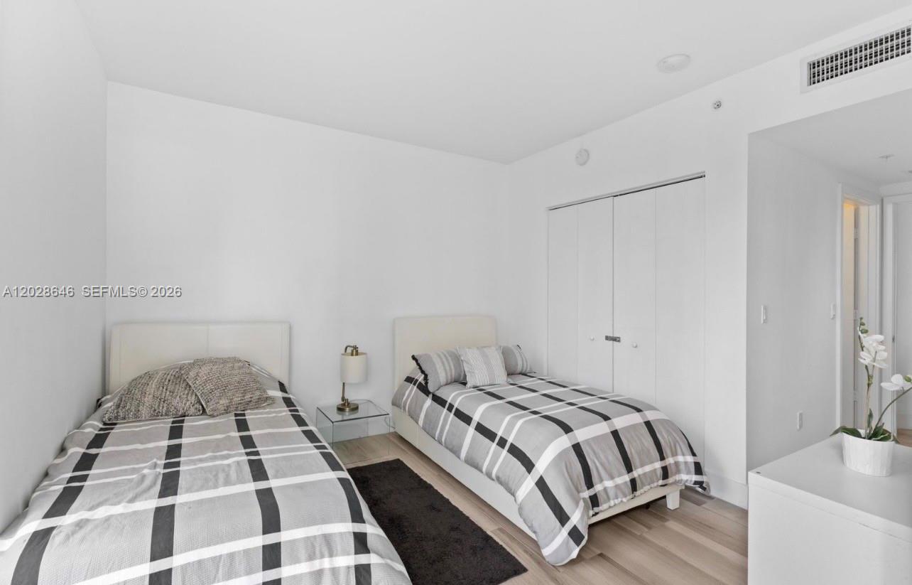 A bedroom features two twin beds with plaid bedding, white walls, and light wood flooring — 1010 SW 2nd Ave # 609, Miami FL 33130, MIAMI, FL