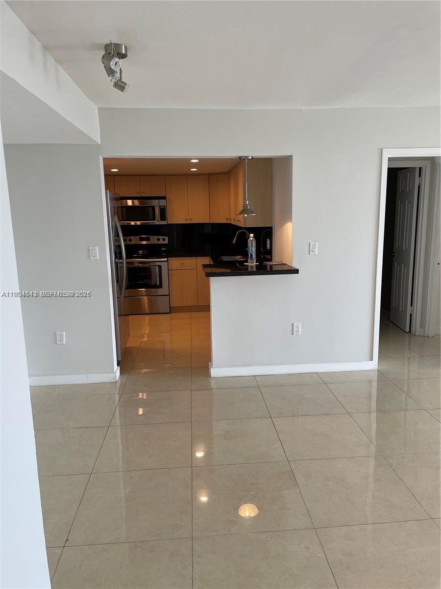 A kitchen with light wood cabinets and black countertops opens to a tiled living area — 13155 Ixora Ct # 901, North Miami FL 33181, NORTH MIAMI, FL