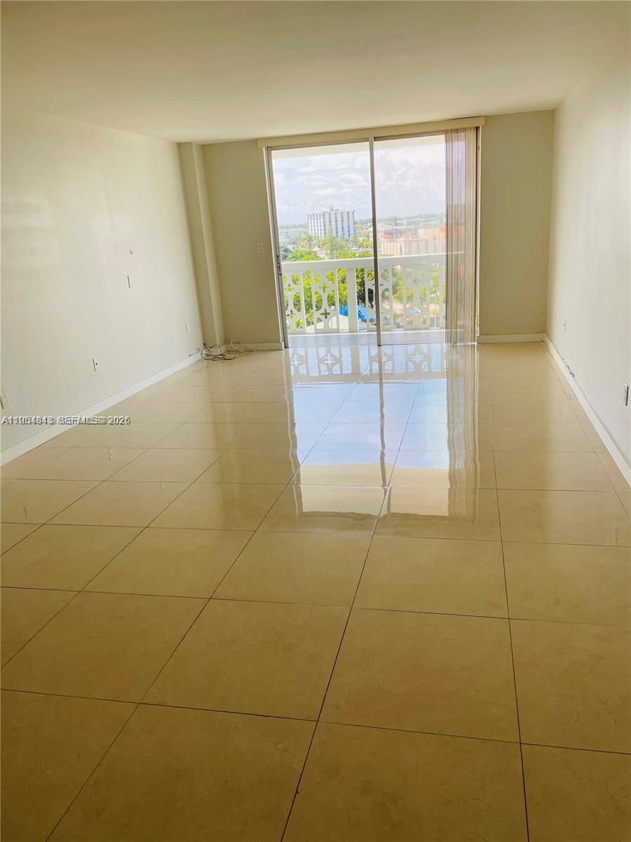 An empty living room features light-colored tile flooring and a sliding glass door to a balcony — 13155 Ixora Ct # 901, North Miami FL 33181, NORTH MIAMI, FL