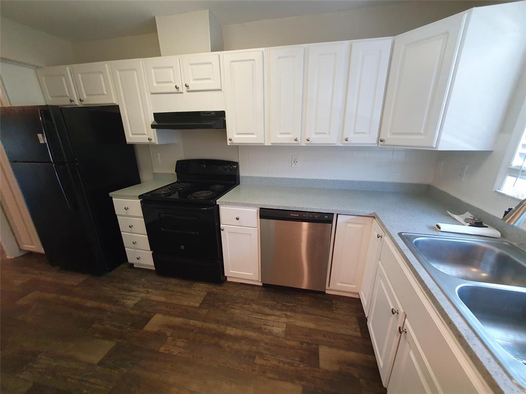 A kitchen features white cabinets, black appliances, a stainless steel dishwasher, and wood-look flooring — 1907 ORANGE BOULEVARD WAY, PALM HARBOR, FL