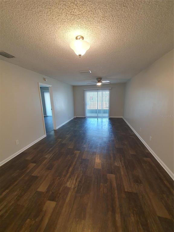 An empty living room features wood-look flooring, a ceiling fan, and sliding glass patio doors — 1907 ORANGE BOULEVARD WAY, PALM HARBOR, FL