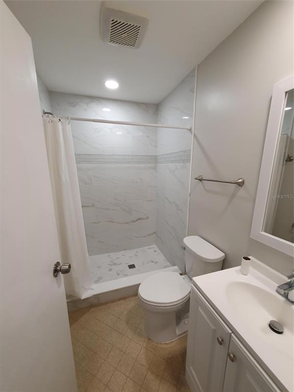 A bathroom features a walk-in shower with marble-look tile, a toilet, and a vanity — 1907 ORANGE BOULEVARD WAY, PALM HARBOR, FL