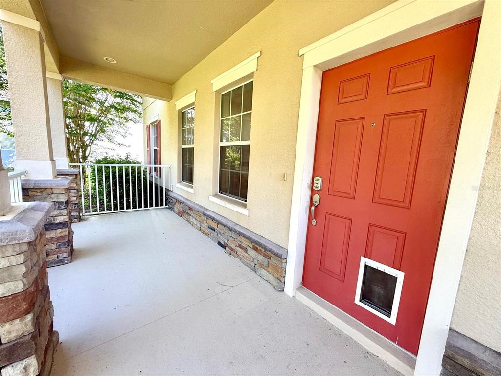 A covered porch features a red front door with a pet door and stone accents — 2054 BLAIRMOOR PLACE, APOPKA, FL