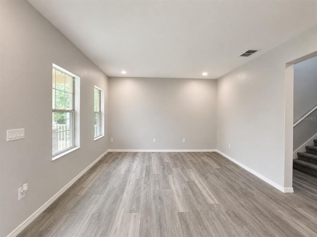An empty room with light gray walls, wood-look flooring, two windows, and a staircase — 2054 BLAIRMOOR PLACE, APOPKA, FL