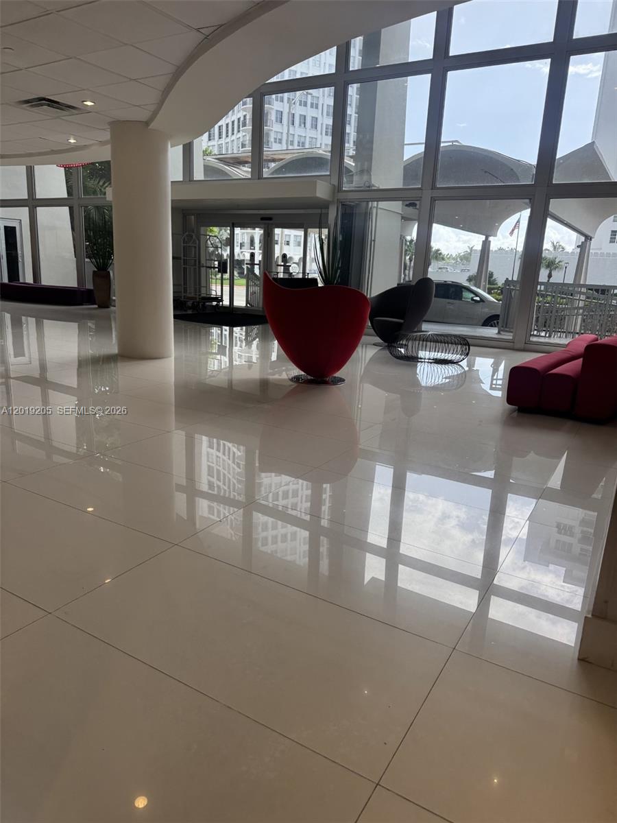 A modern building lobby features white tile floors, floor-to-ceiling windows, and contemporary red seating — 5701 Collins Ave # 511, Miami Beach FL 33140, MIAMI BEACH, FL