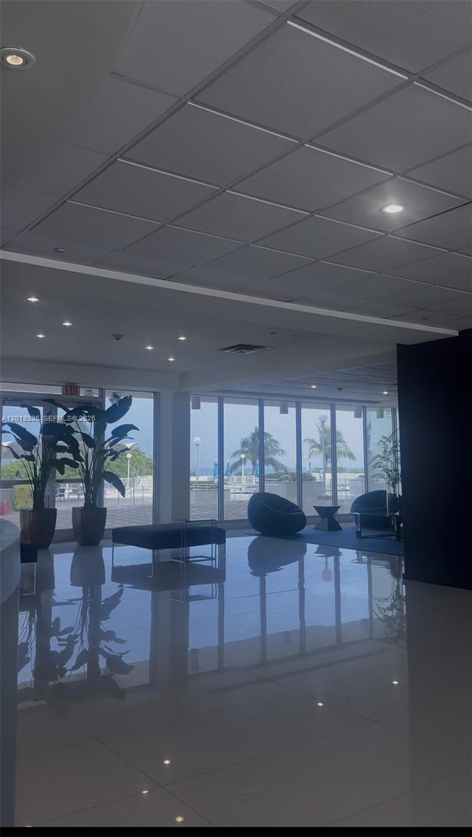 A modern lobby with floor-to-ceiling windows, potted plants, and a polished reflective floor — 5701 Collins Ave # 511, Miami Beach FL 33140, MIAMI BEACH, FL