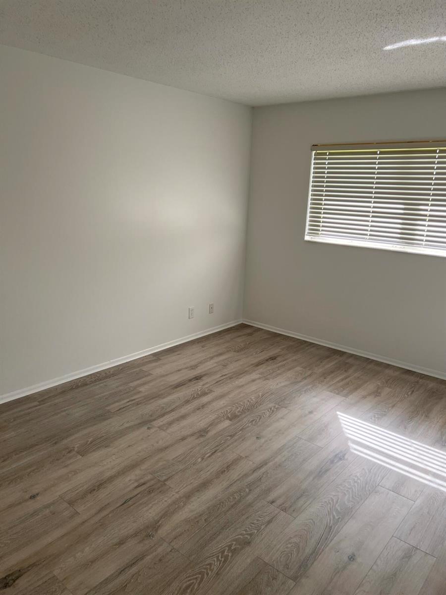 An empty bedroom features light gray walls, wood-look flooring, and a window with white blinds — 2736 Dudley Drive E # I, West Palm Beach FL 33415, WEST PALM BEACH, FL