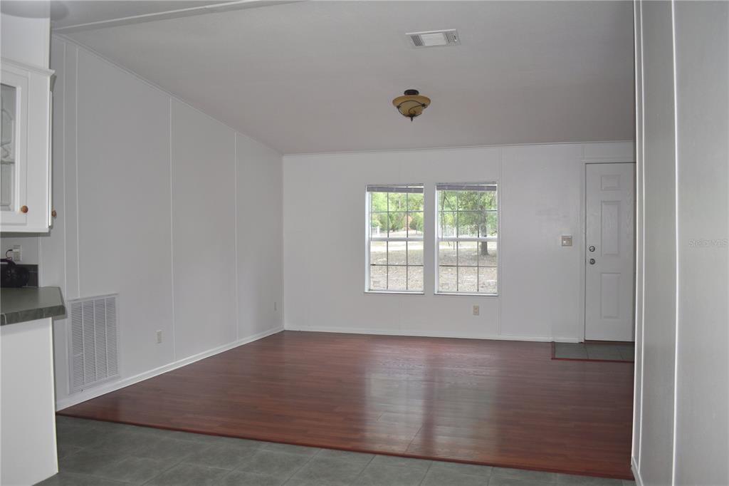 An empty room with wood-look flooring, white walls, two windows, and a white entry door — 8231 NE 111TH STREET, BRONSON, FL