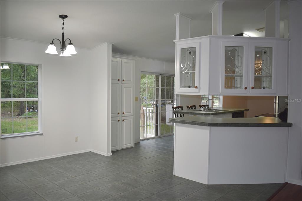 A kitchen and dining area with white cabinets, tile flooring, and a sliding glass door — 8231 NE 111TH STREET, BRONSON, FL