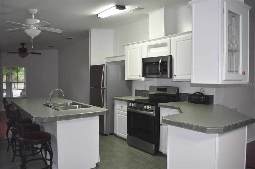 A kitchen features white cabinets, stainless steel appliances, a tiled island, and green countertops — 8231 NE 111TH STREET, BRONSON, FL