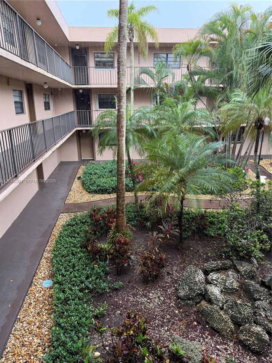 An outdoor courtyard with tropical plants and palm trees surrounded by a multi-story apartment building — 10975 SW 107th St # 302, Miami FL 33176, MIAMI, FL