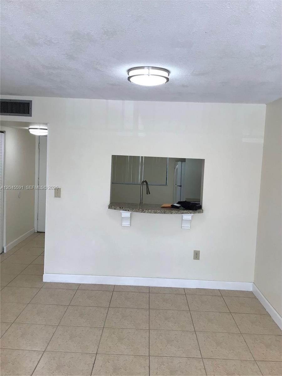 A room with beige tile flooring features a kitchen pass-through window with a granite counter — 10975 SW 107th St # 302, Miami FL 33176, MIAMI, FL