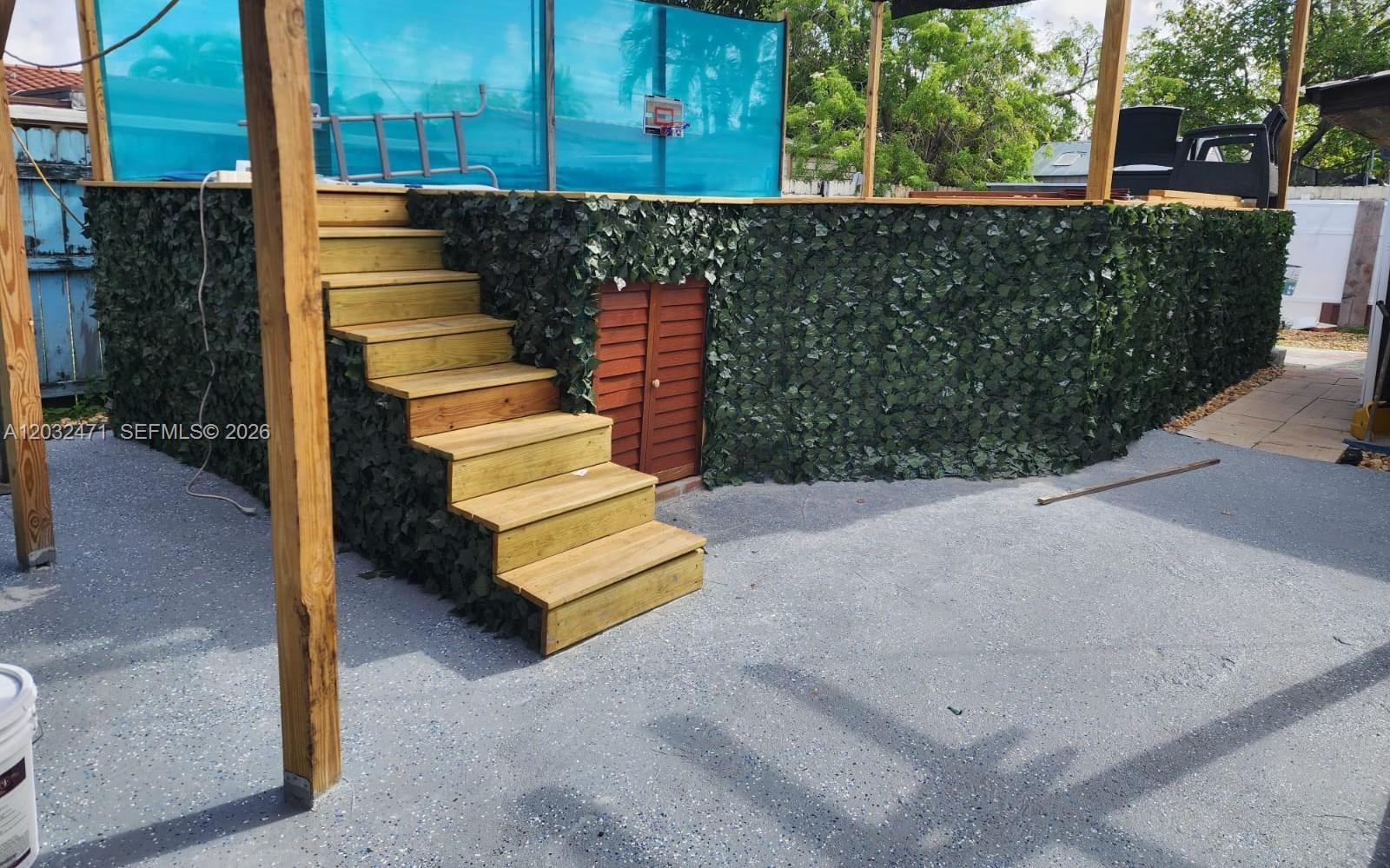 An elevated wooden deck with stairs and artificial ivy siding sits above a concrete patio — 11267 SW 7th St, Sweetwater FL 33174, SWEETWATER, FL