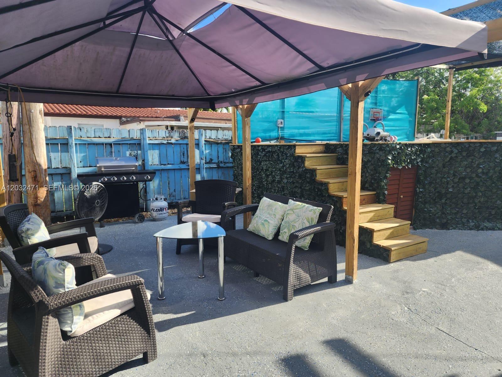 An outdoor patio features a gazebo, wicker furniture, a grill, and wooden stairs leading upward — 11267 SW 7th St, Sweetwater FL 33174, SWEETWATER, FL