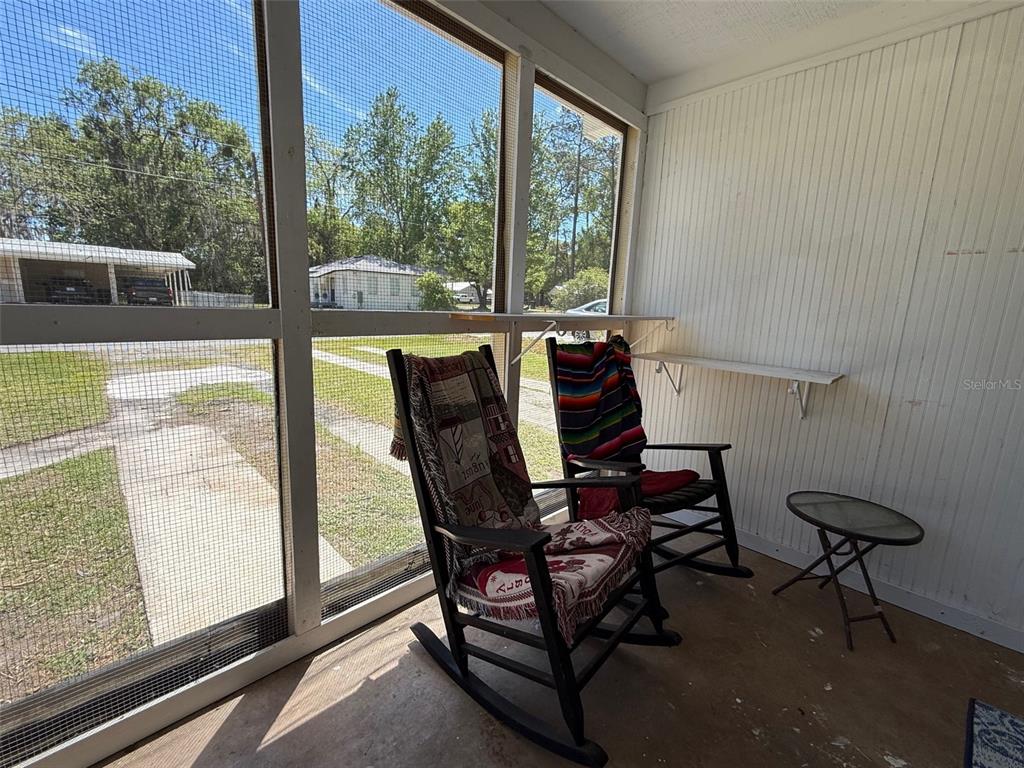 A screened-in porch features two rocking chairs, a small side table, and white paneled walls — 1135 NEIL COURT, STARKE, FL