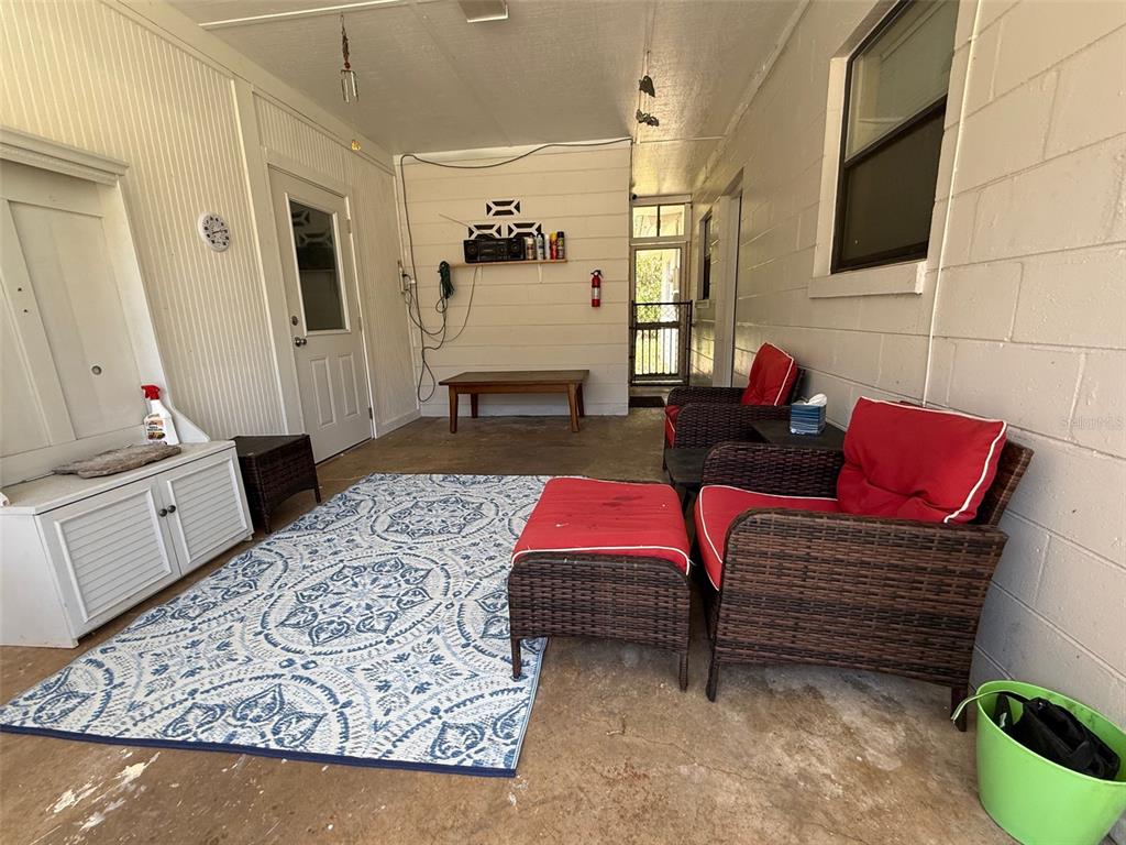 A covered patio features a patterned area rug, wicker furniture with red cushions, and concrete flooring — 1135 NEIL COURT, STARKE, FL