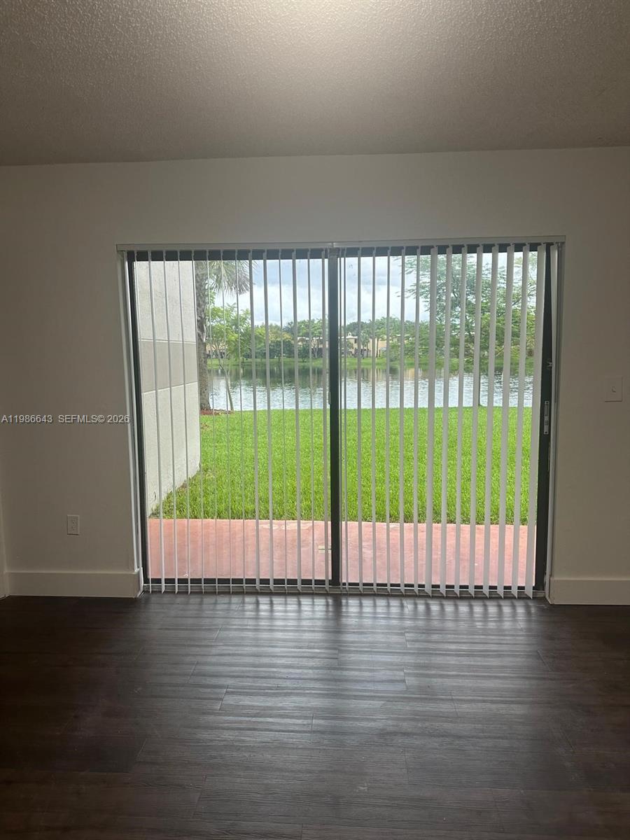 A room with dark wood-look flooring features a sliding glass door overlooking a lake — 9777 Nob Hill Ct # 9777, Sunrise FL 33351, SUNRISE, FL