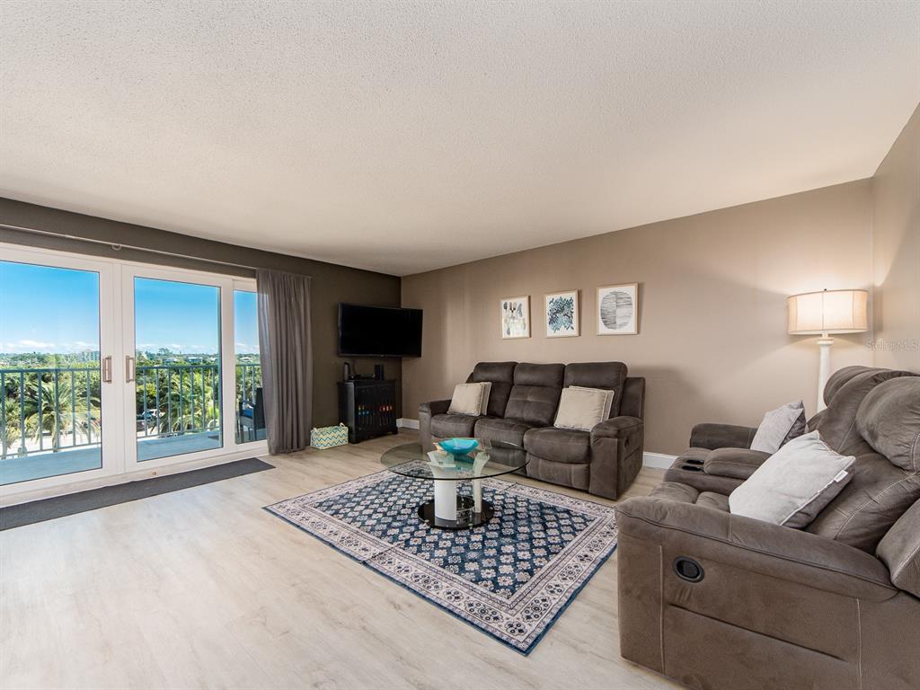 A living room features gray sofas, a glass coffee table, and a balcony with views — 19610 GULF BOULEVARD UNIT 303, INDIAN SHORES, FL