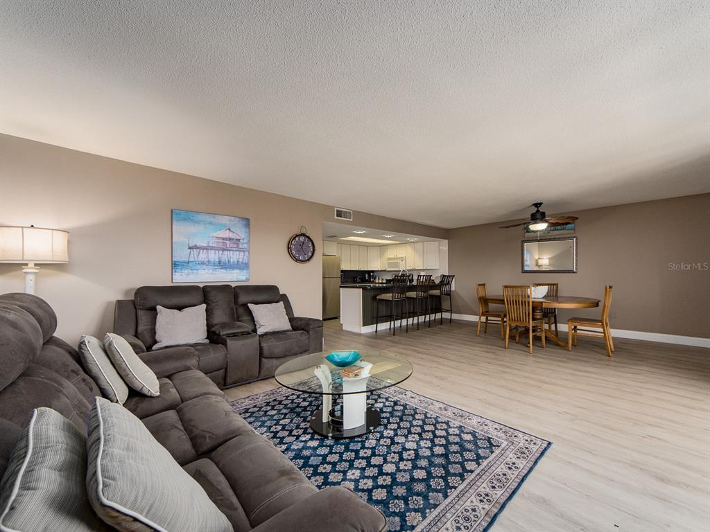 A living room and dining area with gray furniture, a blue rug, and kitchen bar seating — 19610 GULF BOULEVARD UNIT 303, INDIAN SHORES, FL