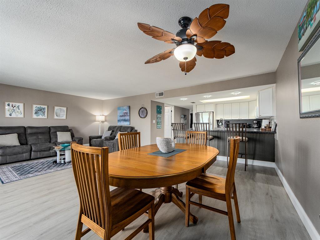 A dining area with a wooden table and chairs opens into a living room and kitchen — 19610 GULF BOULEVARD UNIT 303, INDIAN SHORES, FL