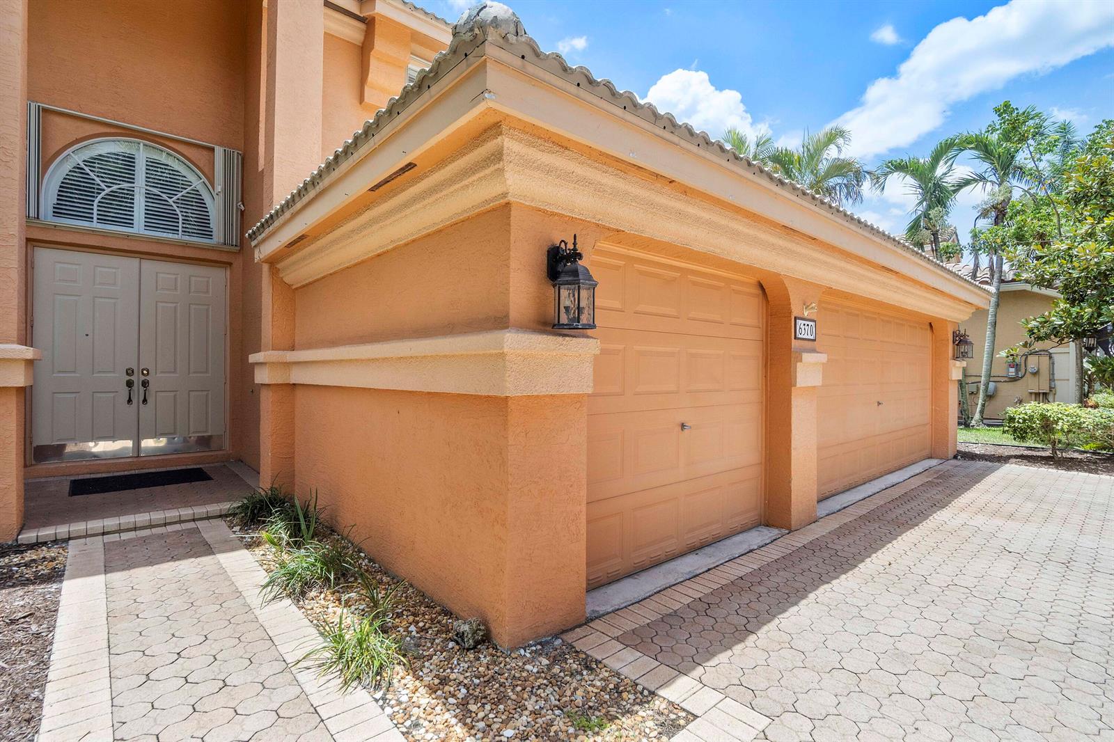 An exterior view of a peach-colored house with a two-car garage and paved driveway — 6370 Stonehurst Circle, Lake Worth FL 33467, LAKE WORTH, FL